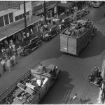 trucks carrying tons of scarp metal through a town during a WWII scrap drive