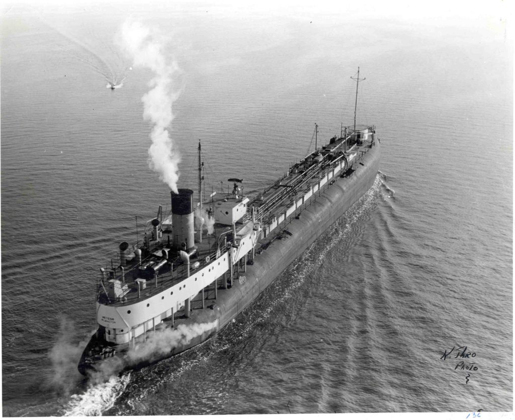 A black and white photo of a whaleback ship converted to be an oil tanker steaming across a lake