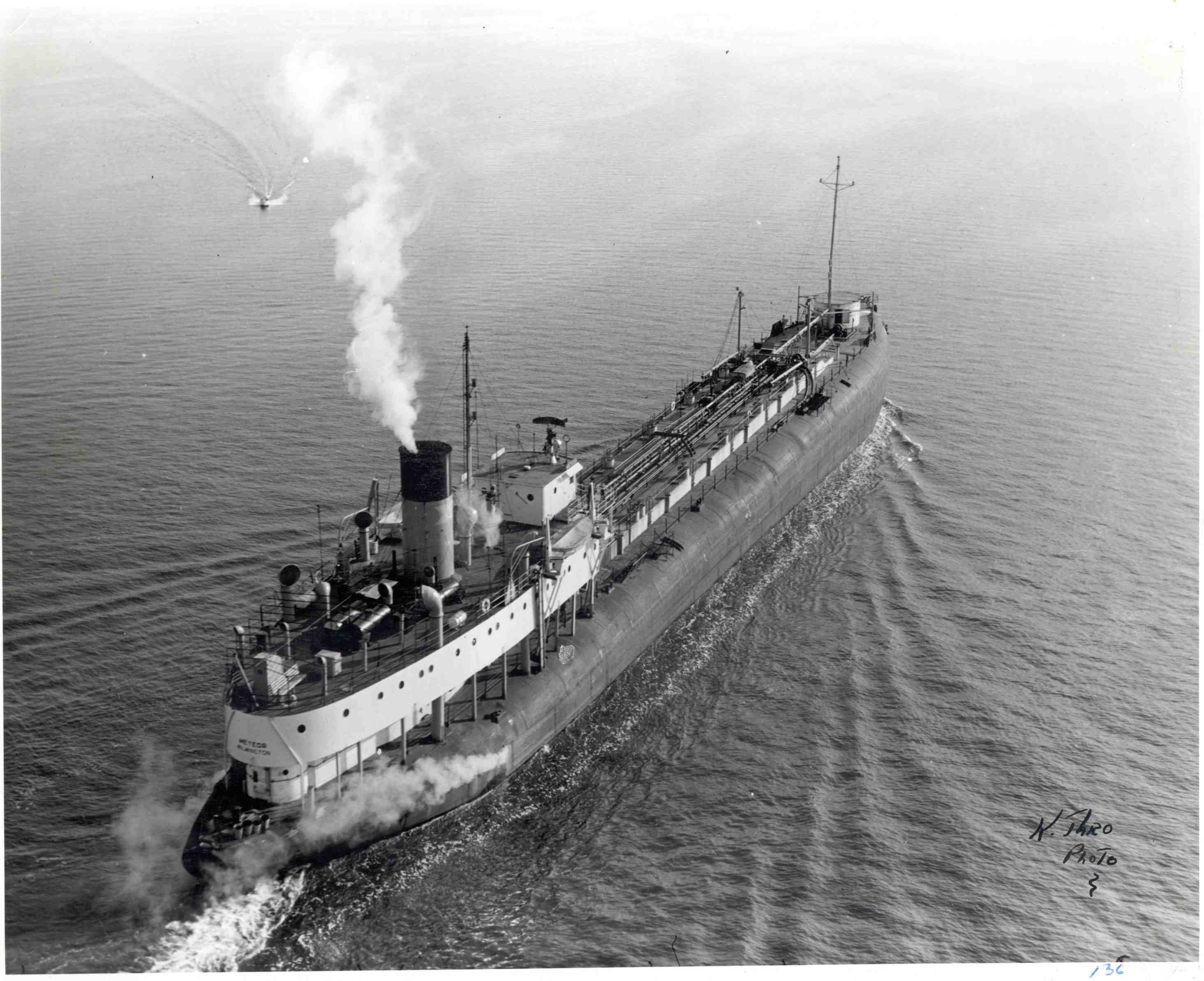 A black and white photo of a whaleback ship converted to be an oil tanker steaming across a lake 