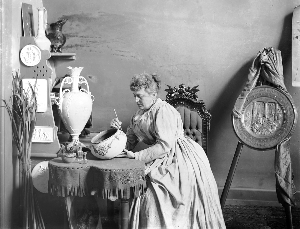 A portrait of a woman painting a ceramic bowl at a table.