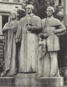 Sculpture showing three figures, the central figure is a french priest with a Native American man to his right and a french colonial man to his left
