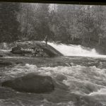 a black and white photo of a man fly fishing in the Wolf River standing in the rapids