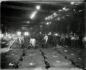 A black and white image of the shop floor of a factory showing workers posing with machines