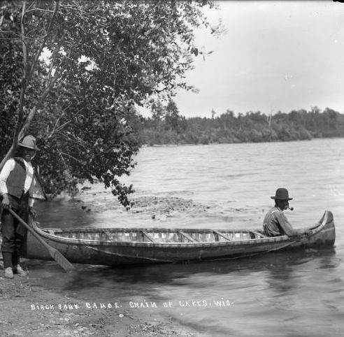 Two men and a birch bark canoe beside a lake