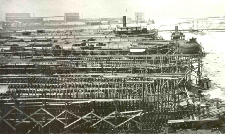 A black and white photograph showing the boat yards where several whaleback ships are under construction, now only visible a steel ribs.