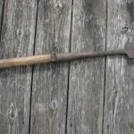 a color photograph of a metal tool with a rounded edge and a wooden handle about two feet long