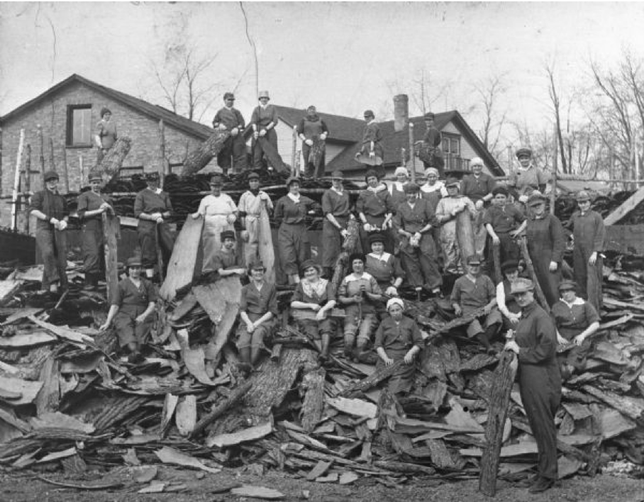 A picture of several men and women standing on a pile of hemlock bark holding bark spuds