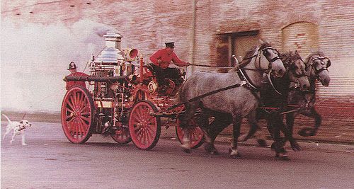 A dalmatian running alongside a fire engine.